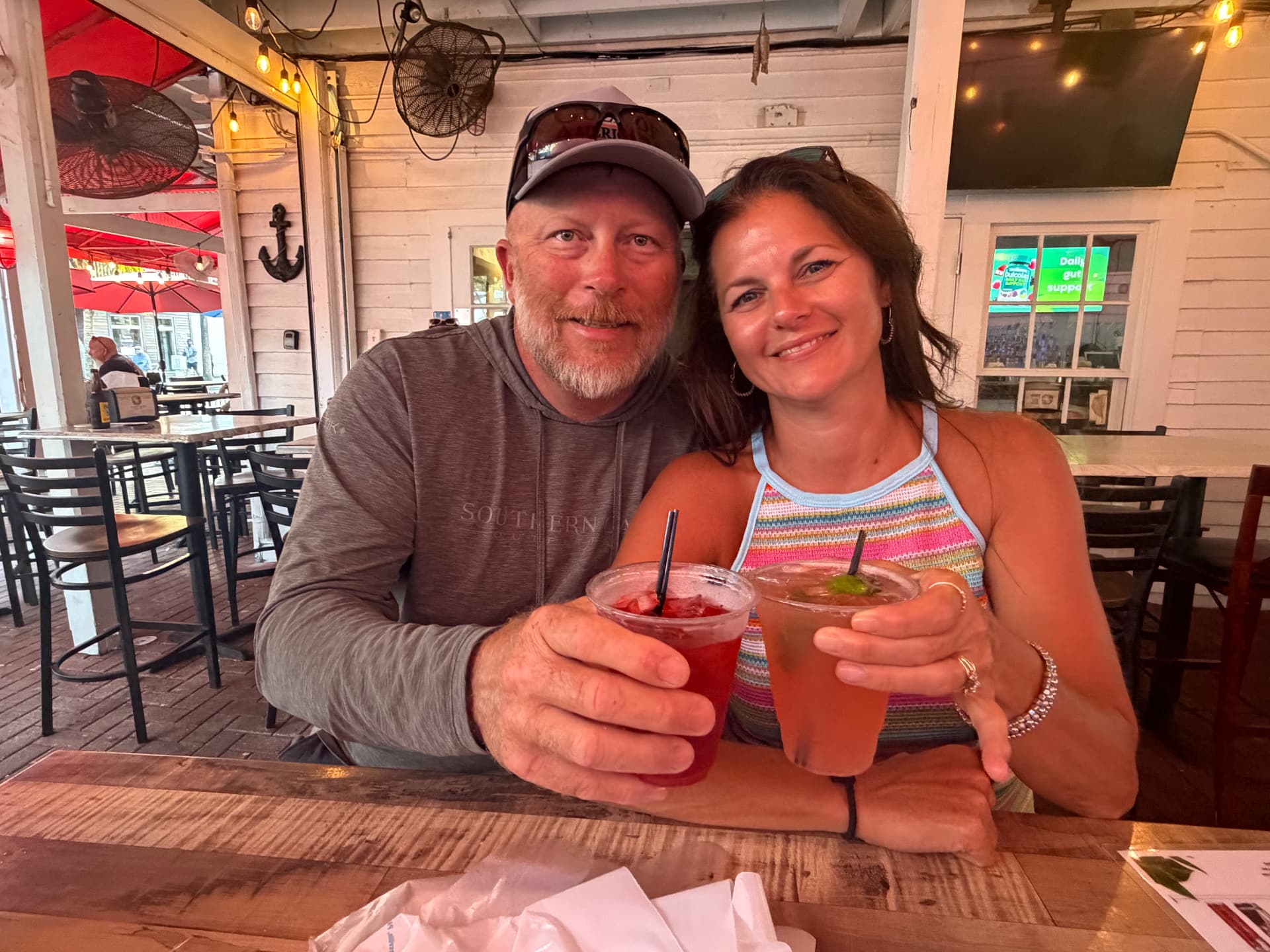 Randy and Angie, the owners of The Rusty Hook Riverhouse, raising a drink together on a waterfront porch in Old Homosassa, Florida