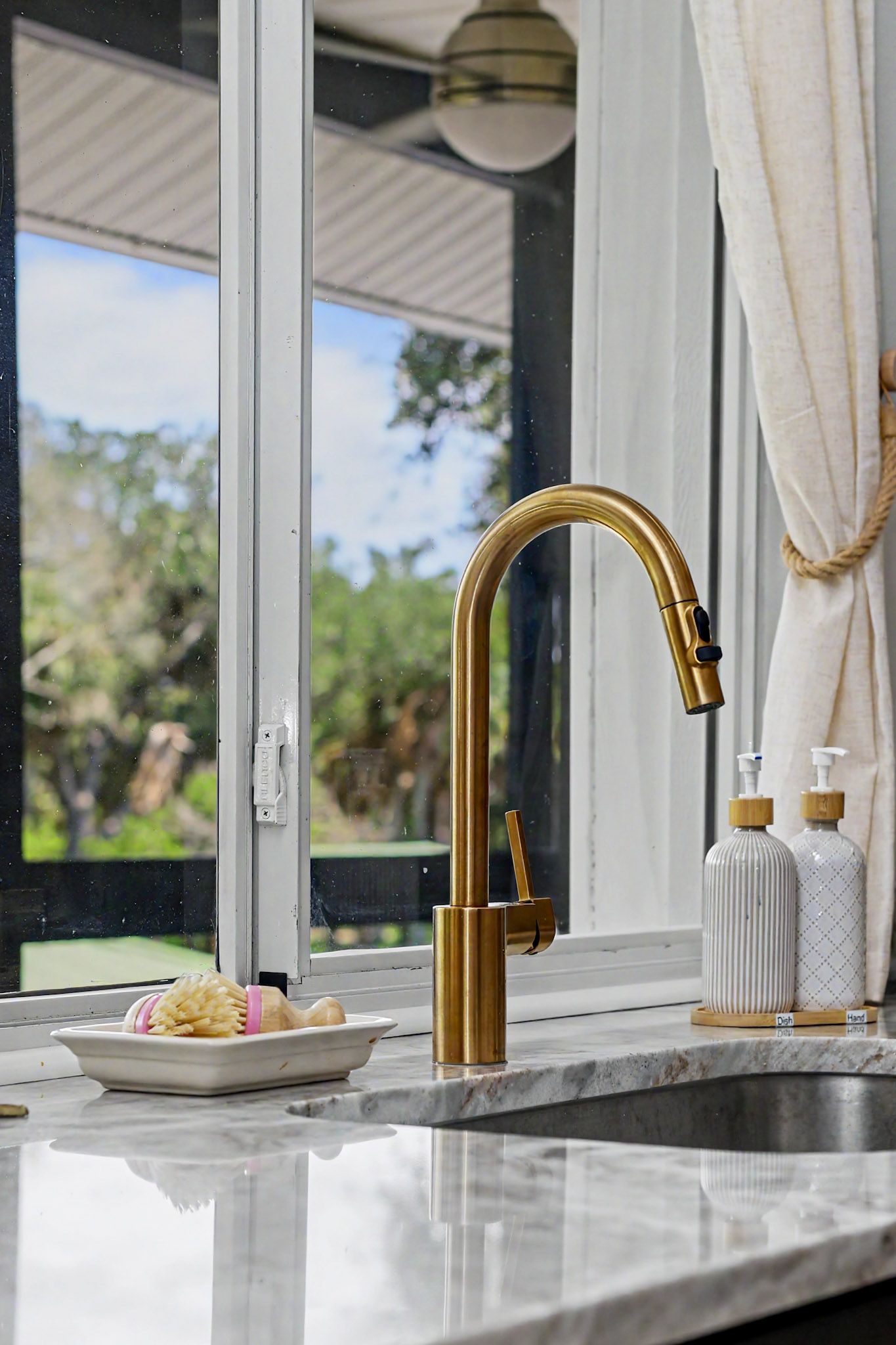 Brass gooseneck faucet over the kitchen sink with the greenery of the waterway through the window