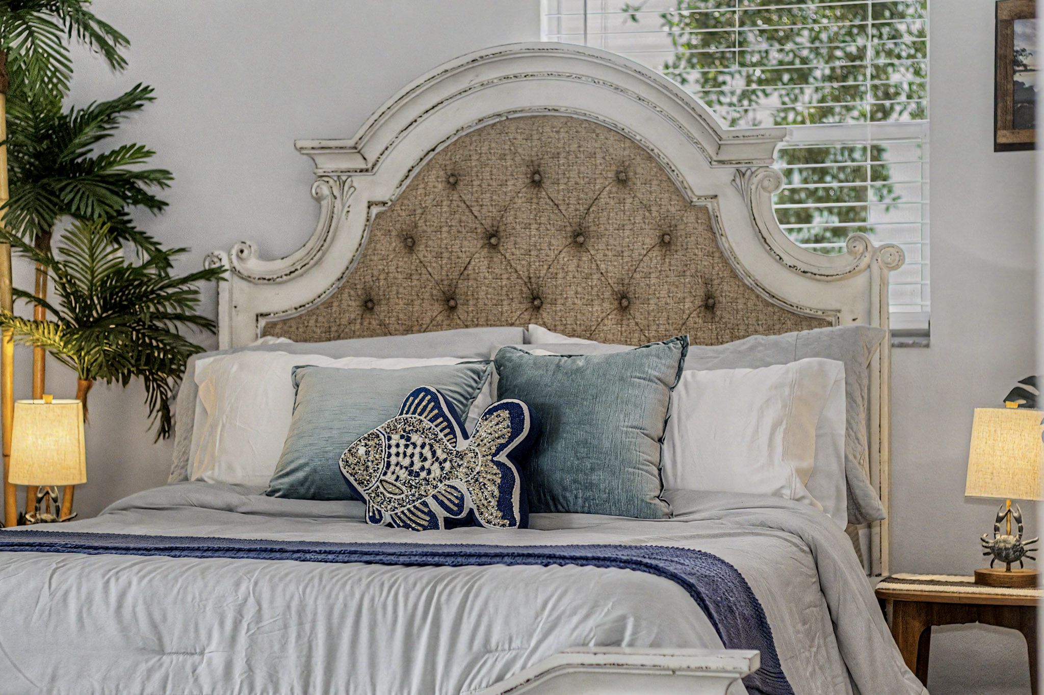 The Captain's Quarters (the primary bedroom) with a tall carved headboard, white linens and blue textiles beside a bright window